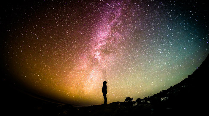 Silhouette of a man staring up at the Milky Way night sky