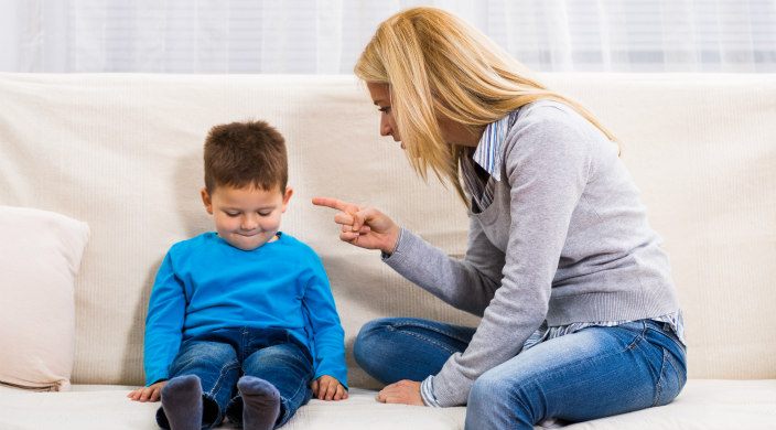 Mother and preschool child on a couch; mother scolding and pointing her finger at the child