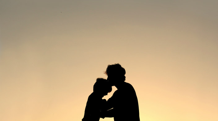 Silhouette of a parent with his or her forehead touching that of a child 