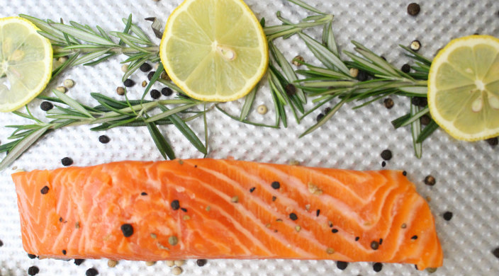 Plank of salmon garnished with peppercorns lemon slices and herbs 