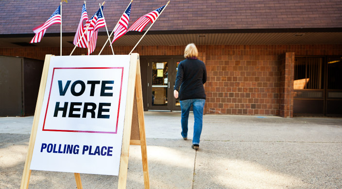 VOTE HERE sign outside a polling place where a women is walking through the doors