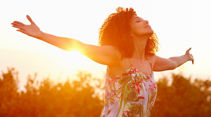 Woman with outstretch arms; eyes closed, face skyward; sun and trees in the background