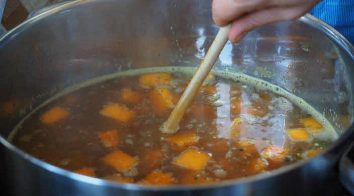 Hand using a wooden spoon to stir a pot of soup 