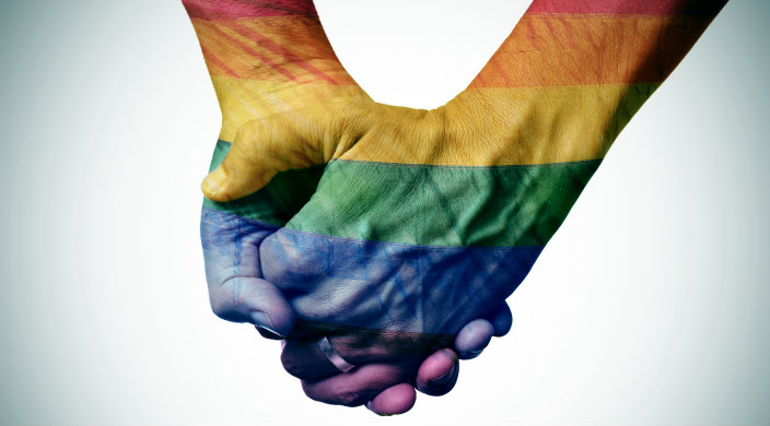 Two men holding hands; hands and wrists are in Pride stripes