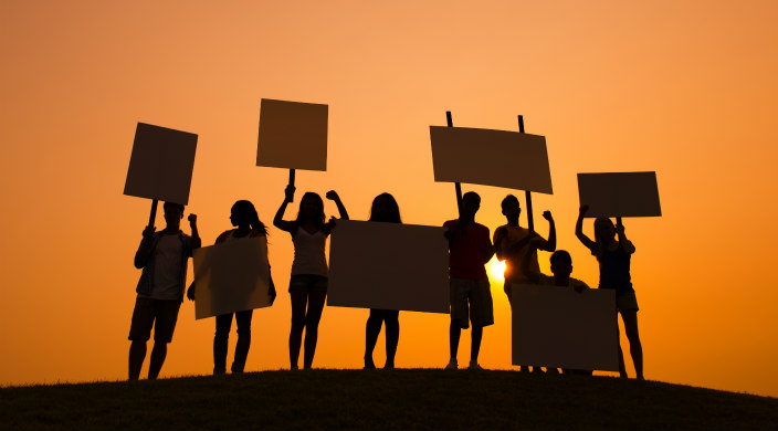Row of protesters with signs in shadow; bright sun behind them