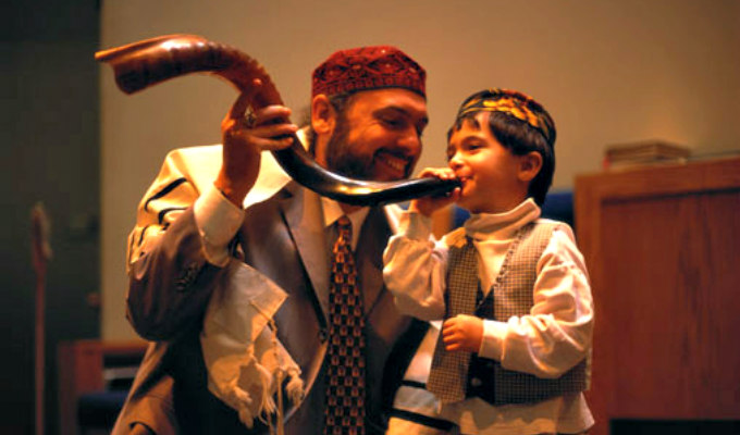 Rabbi teaching a young boy how to blow a shofar 