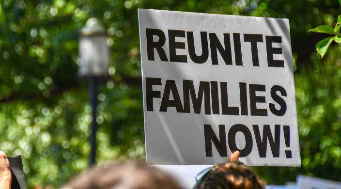 Protest sign held overhead that says: Reunite Families Now