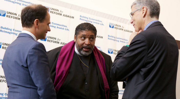 Rev William J Barber II speaks to Rabbi Jonah Dov Pesner and Rabbi Rick Jacobs in front of a Union for Reform Judaism banner