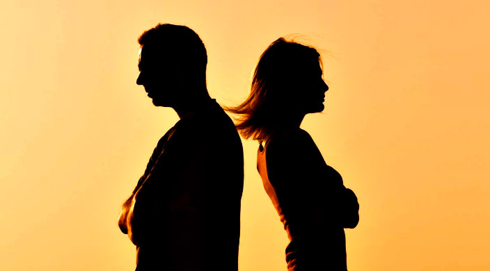 Silhouette of a man and a woman with their backs facing one another as if arguing