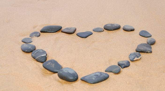 Flat stones laid out to form the shape of a heart on wet beach sand 
