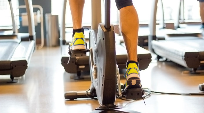 Back of the legs and feet of a person on a stationary bicycle in a gym