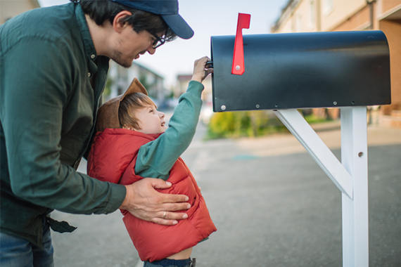 A dad helps his son put a letter into a mailbox