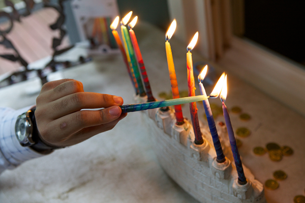an image of a hand holding the shamah and lighting the other eight candles on a menorah