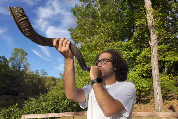 A young person blowing the shofar outdoors