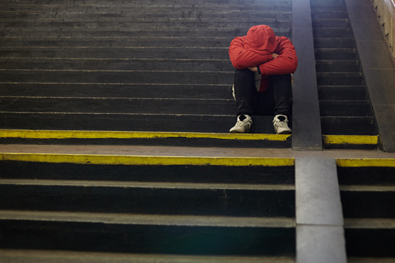 Photo of a person sitting by themselves on stairs with their arms folded and head down on knees