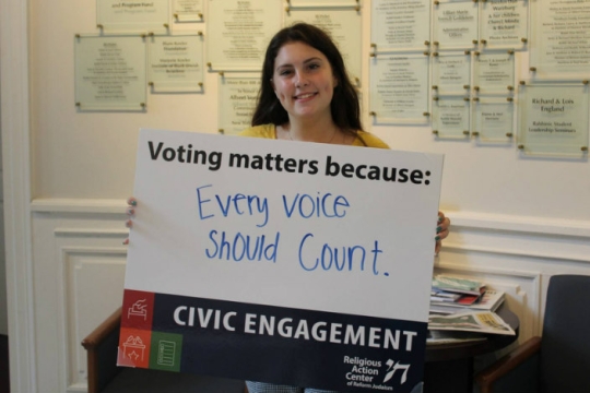Smiling teen girl holding a sign that says VOTING MATTERS BECAUSE EVERY VOTE SHOULD COUNT