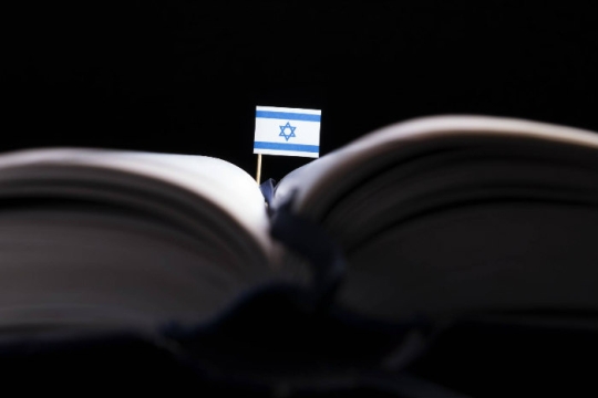 Small Israeli flag sticking out of a textbook in dark lighting