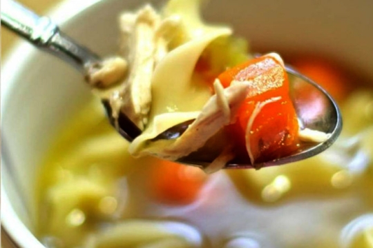 Spoonful of chicken soup hovering over a bowl of it 