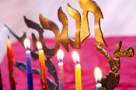 Closeup of six lit candles on a Hanukkah menorah with a pink background