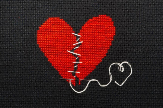Cross stiched image of a broken heart being sewn back together with white thread