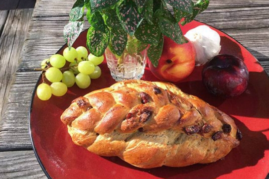 Pumpkin cranberry challah on a red plate with a plant and apples and grapes 