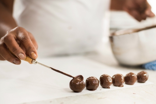 Womans hand making chocolate covered charoset balls on a white counter surface