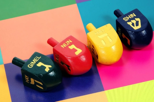 Four colorful wooden dreidels on a brightly colorblocked surface