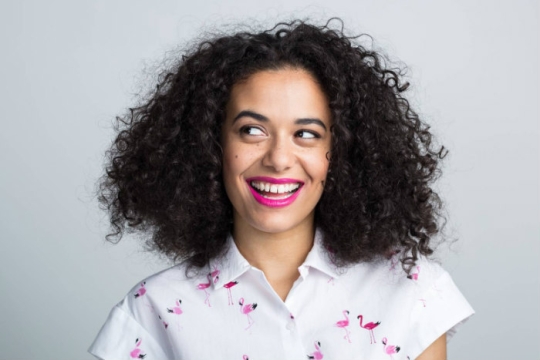 Smiling curly haired woman looking out of frame as if asking a question