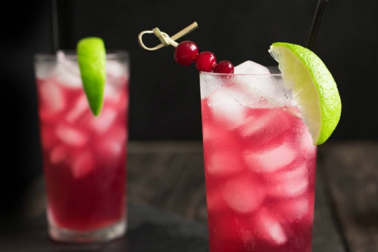 Red drink in a glass with ice cubes and a lime wedge garnish