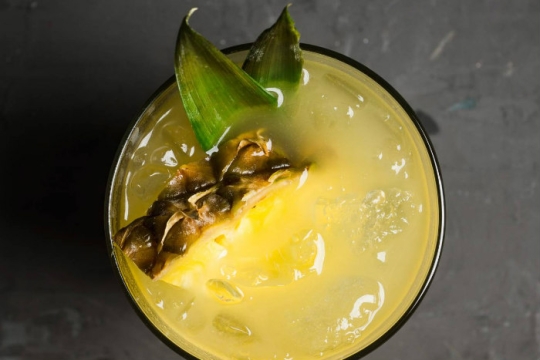 Aerial view of a yellow cocktail topped with a pineapple wedge
