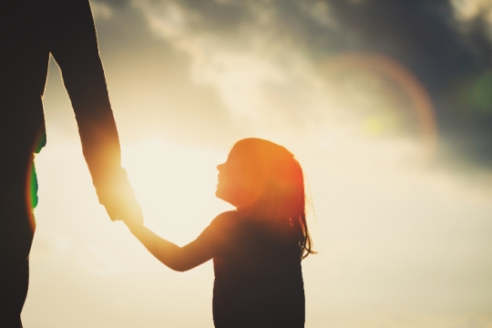 Profile of a young children looking up at an adult while holding their hand