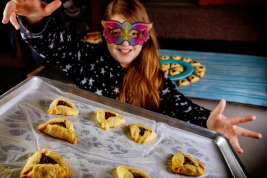 Young girl wearing a mask and holding a tray of hamantaschen 