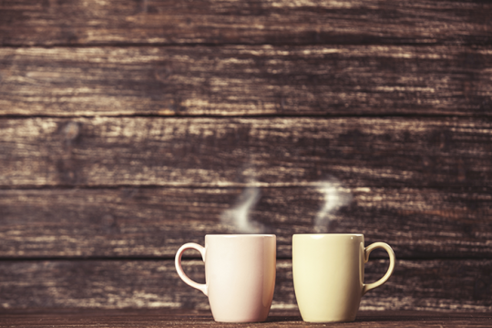 an image of two cups of coffee with steam coming out the top, in front of a wooden background