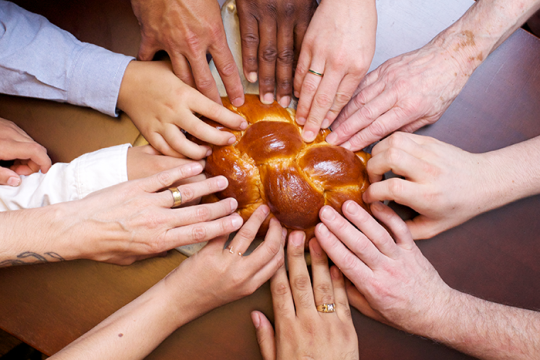 an image of 9 hands touching a challah on a table