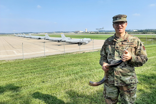 a soldier standing next to an air field with planes behind him while holding a shofar