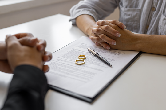 Photo of divorce papers, two wedding rings and two sets of hands