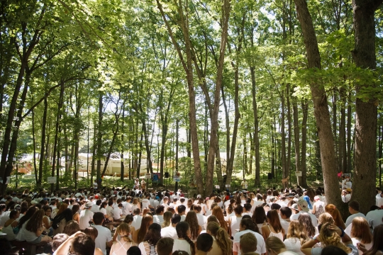 A large group of children all dressed in white in front of tall trees 