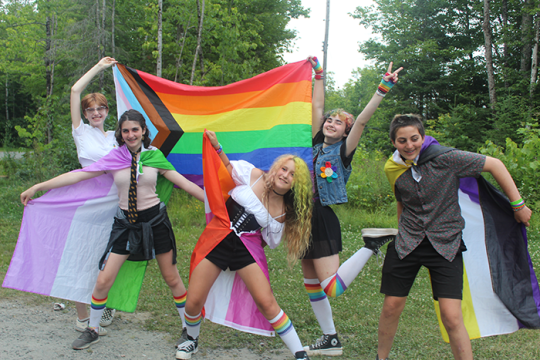 Photo of teens dressed in costume holding a flag for the LGBTQ+ community