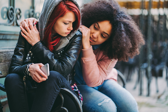 Photo of two girls, one hugging another who looks depressed