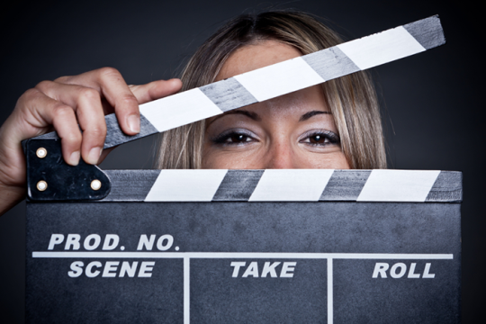 Photo of a woman holding a movie slate in front of her face