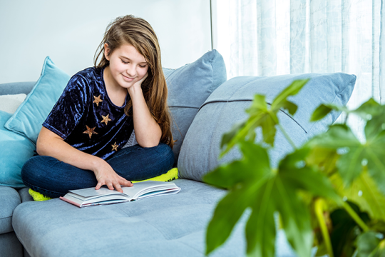 Photo of a girl sitting on a sofa reading a book