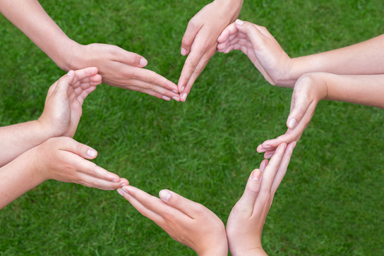 Photo of six hands making the shape of a heart