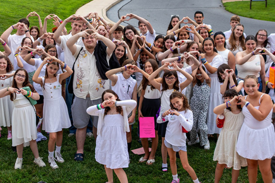 Photo of a group of campers and staff making heart shapes with their hands at the creative arts camp