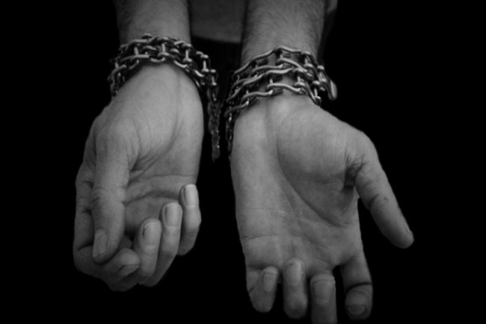 Black and white image of a persons hands bound with chains