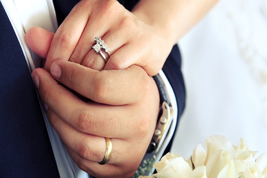 Married couple holding hands, wearing wedding bands