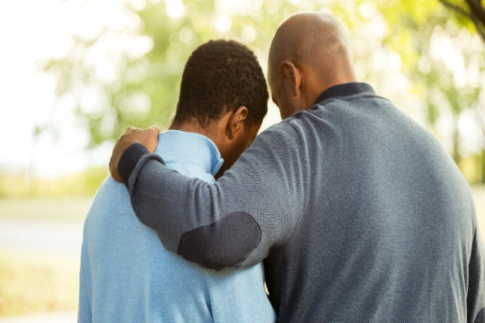 Back view of an older man with his arm around a younger man as if consoling him