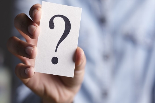 Womans hand holding a piece of paper bearing a question mark