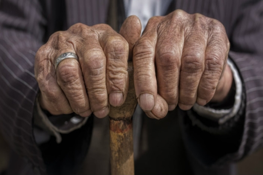 Close up of the hands of an elderly man clutching the top of a cane