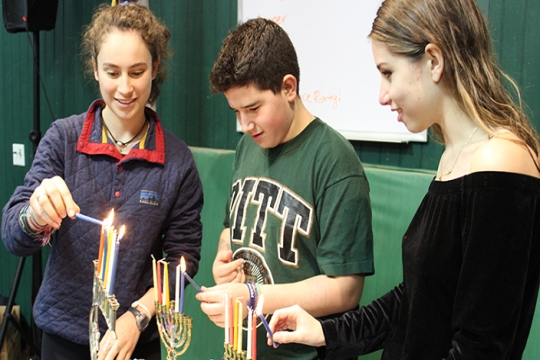 three teens each lighting a hanukkiyah