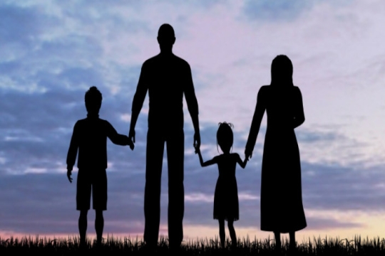 Shadowy profile of two adults and two children holding hands against a sunset